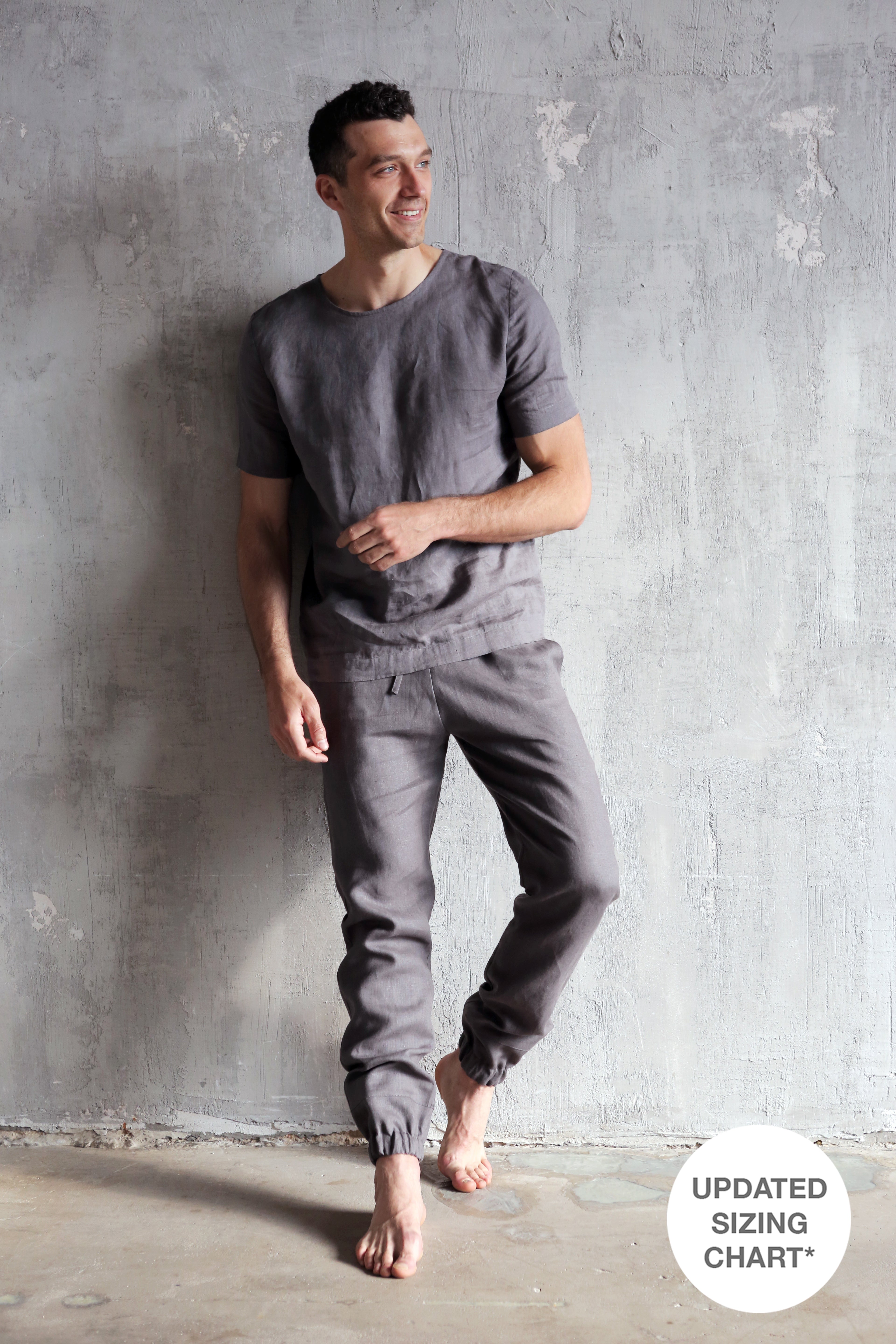 Man wearing a gray t-shirt and pants against a textured gray wall.