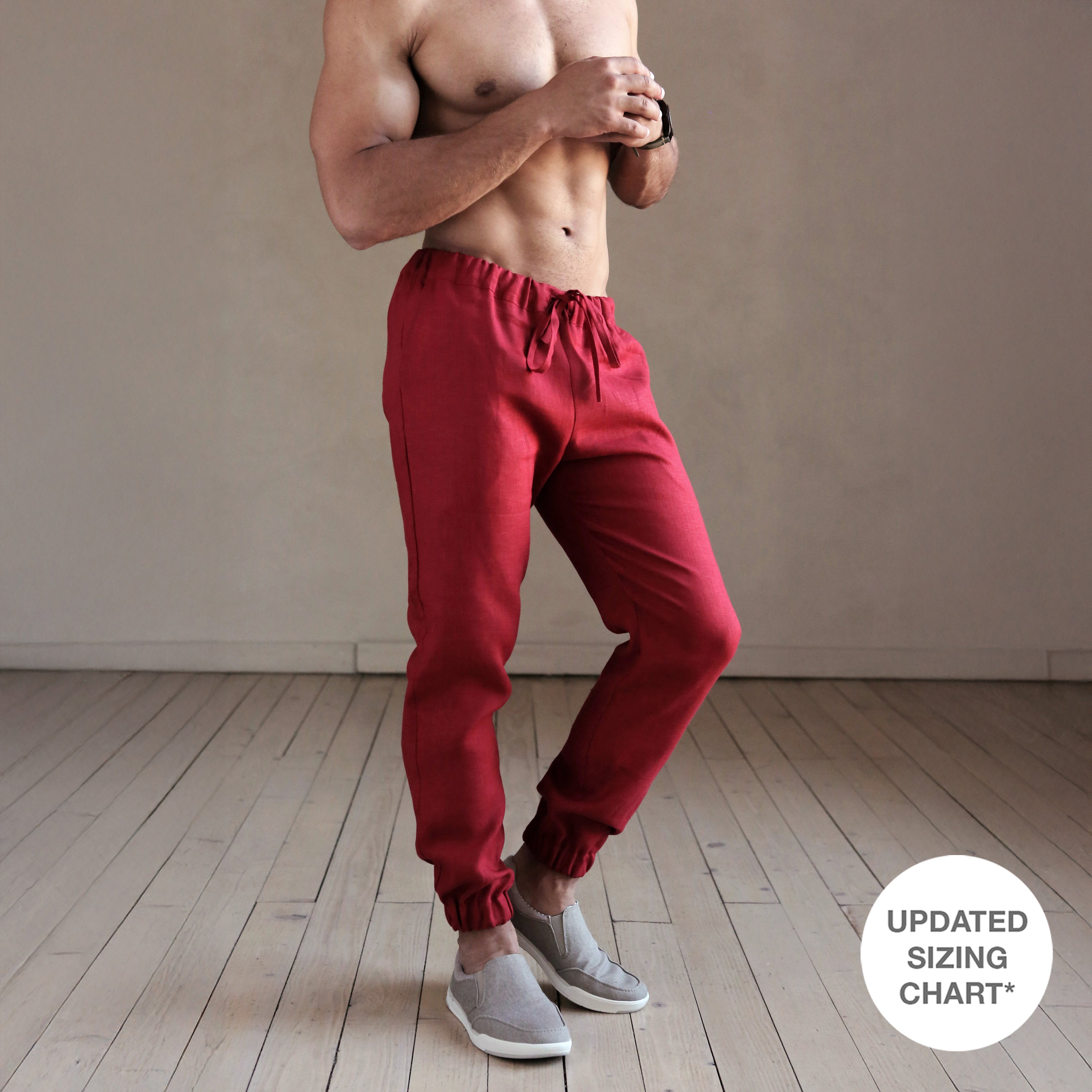Person wearing red sweatpants standing in a room with a wooden floor and beige wall.