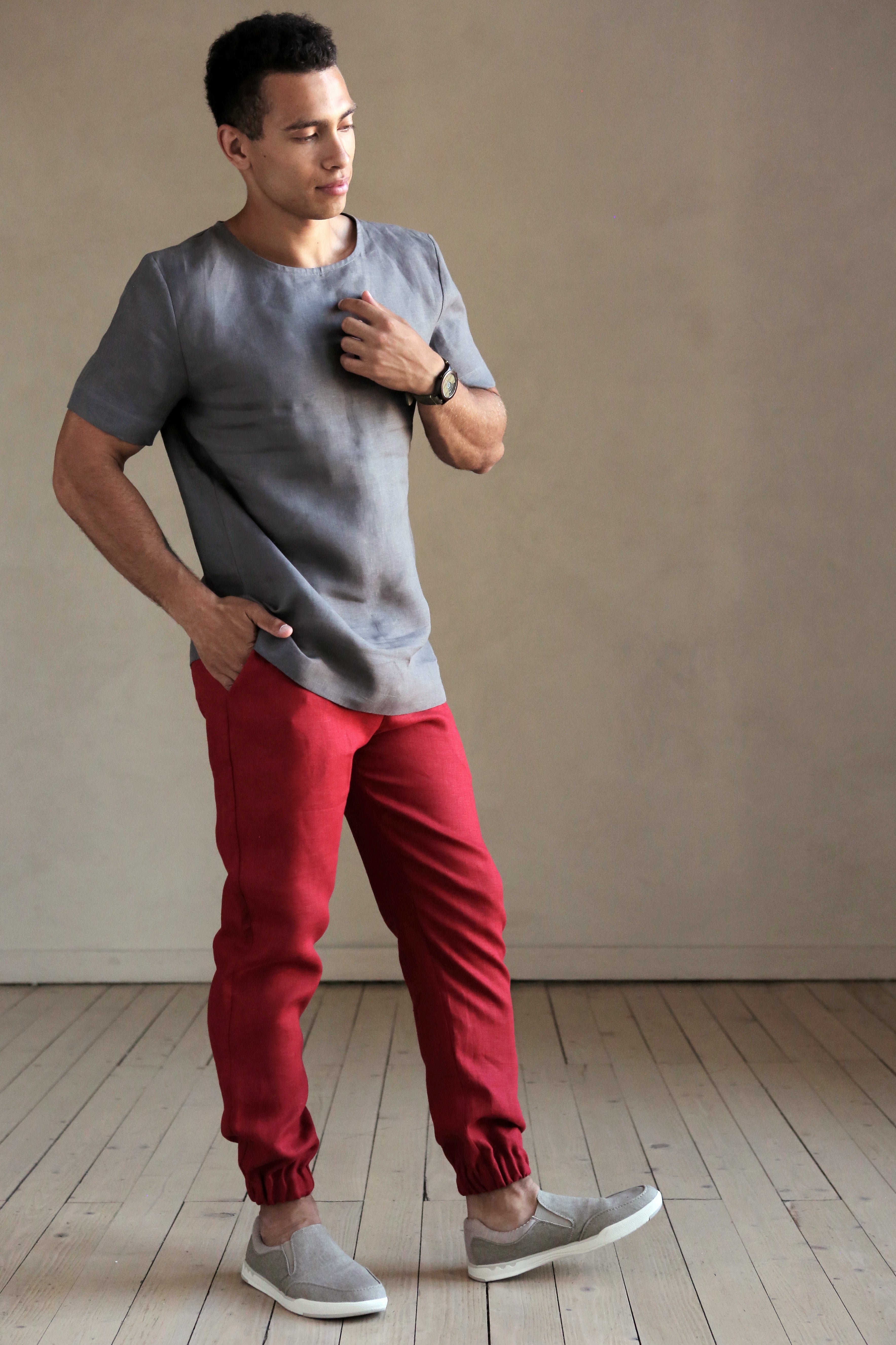 Man wearing a gray shirt and red pants standing against a plain wall.