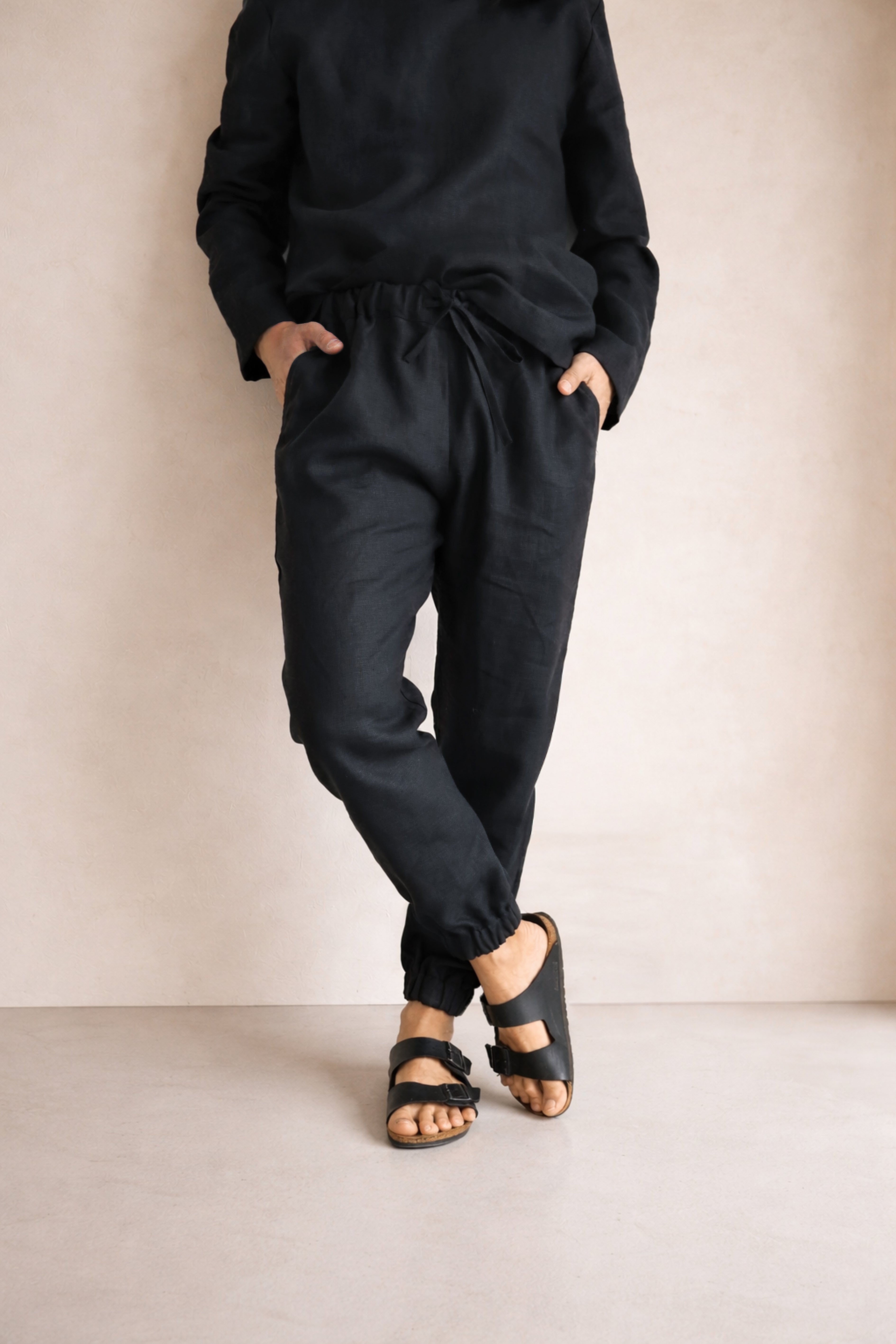 Person wearing black pants and sandals against a beige background