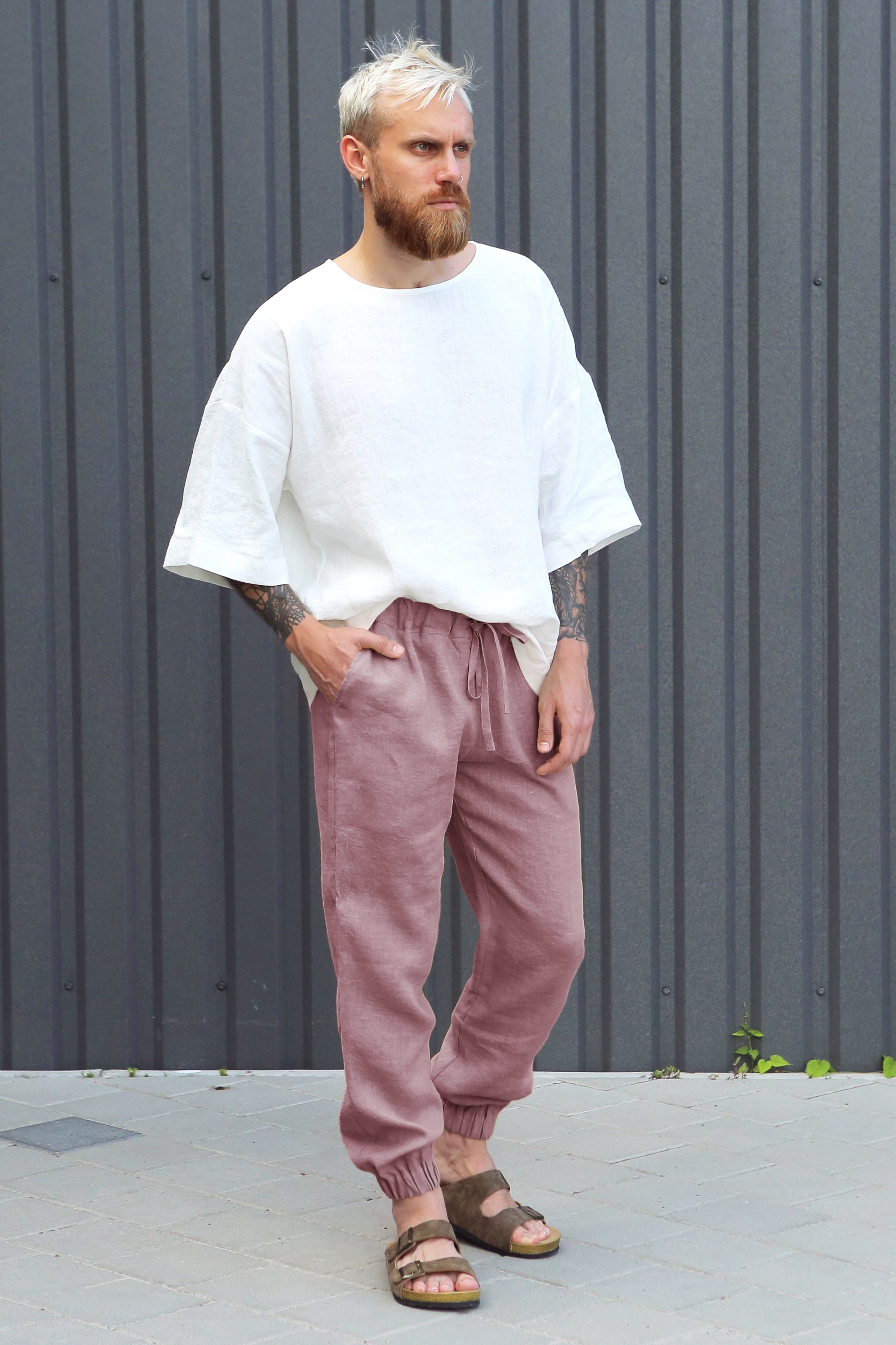 Man wearing a white shirt and latte pants standing against a gray wall.