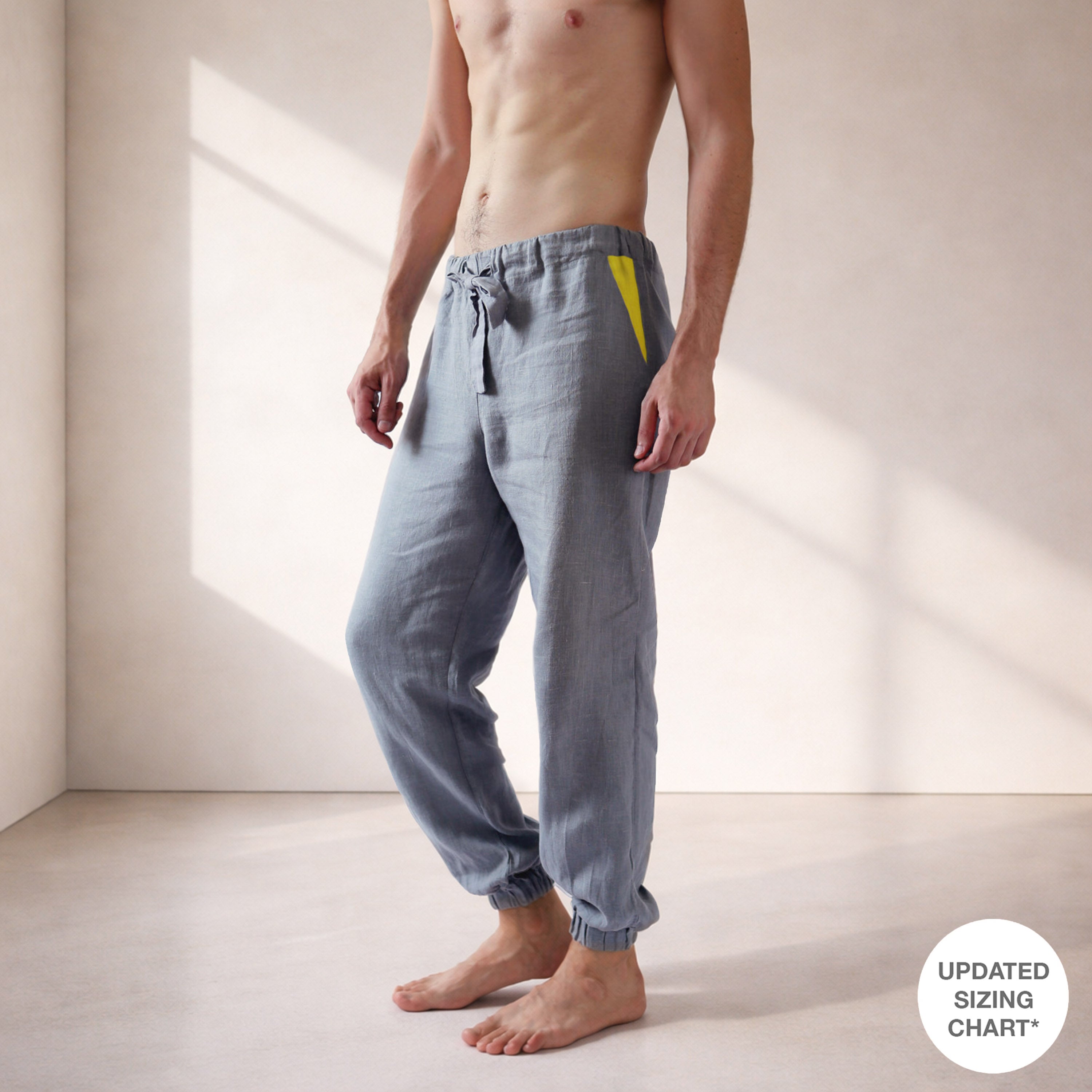 Man wearing gray jogger pants with a yellow patch in a minimalistic setting