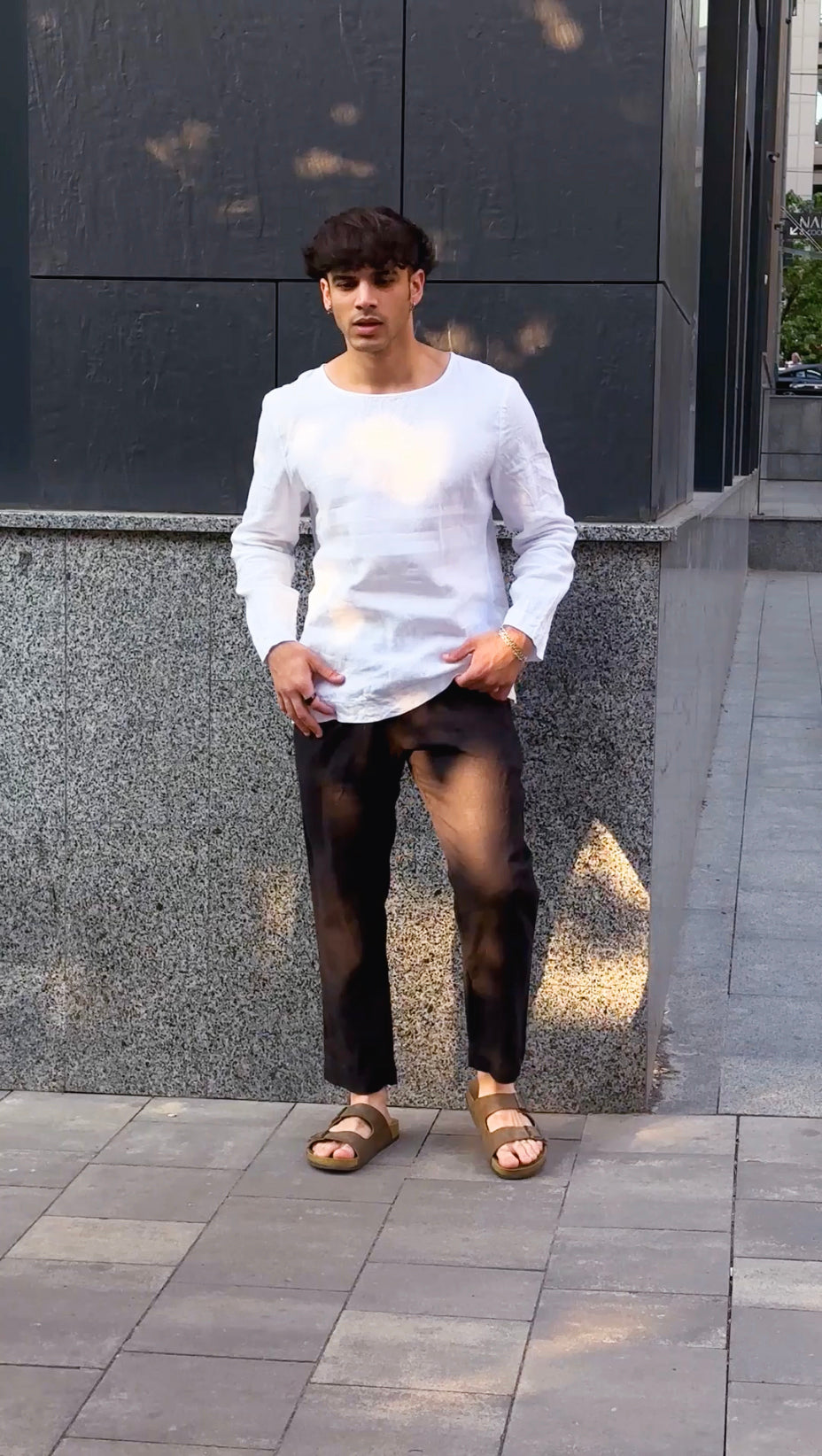 Man wearing black linen pants and white t-shirt in front of the building