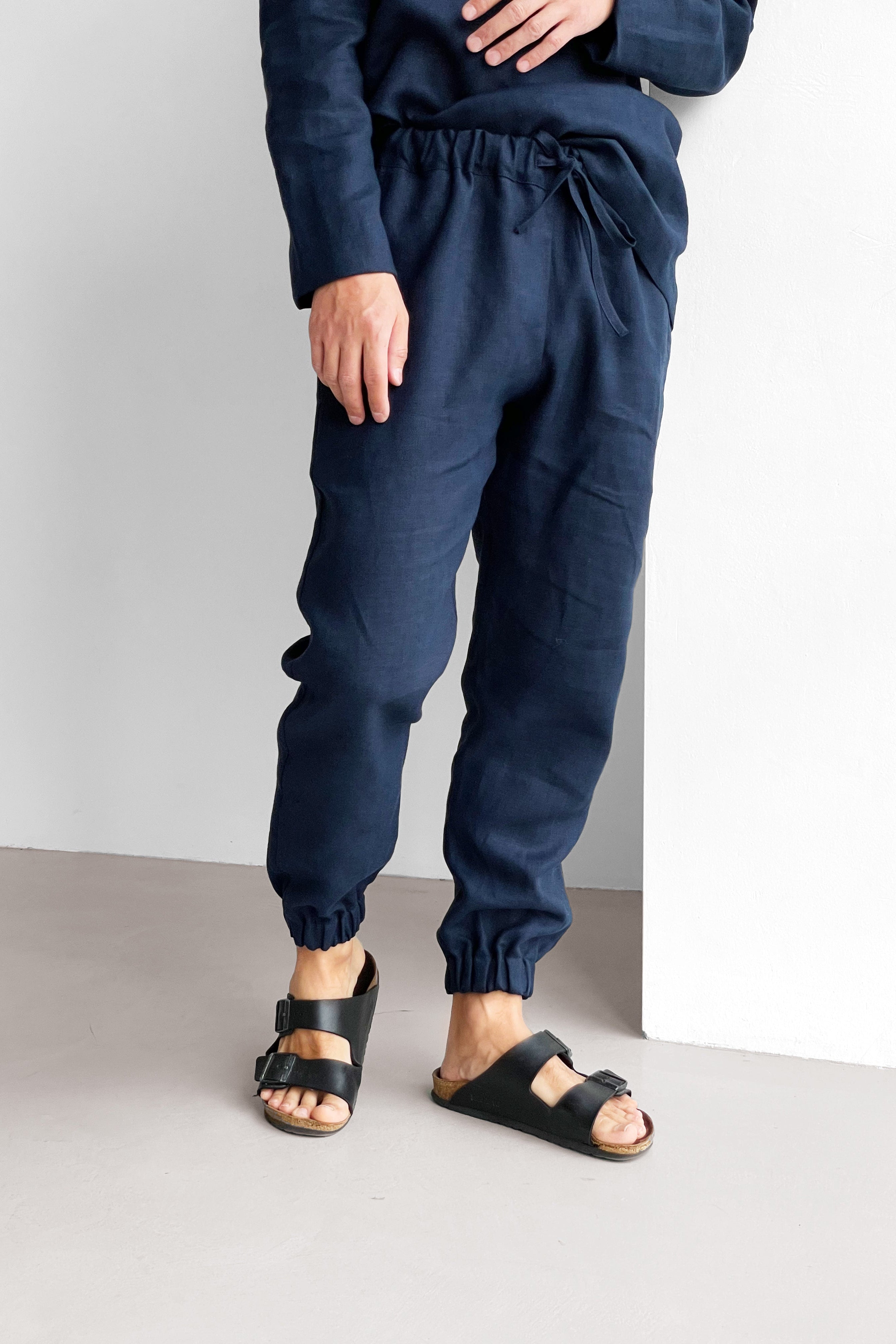 Person wearing navy blue sweatpants and black sandals on a plain background