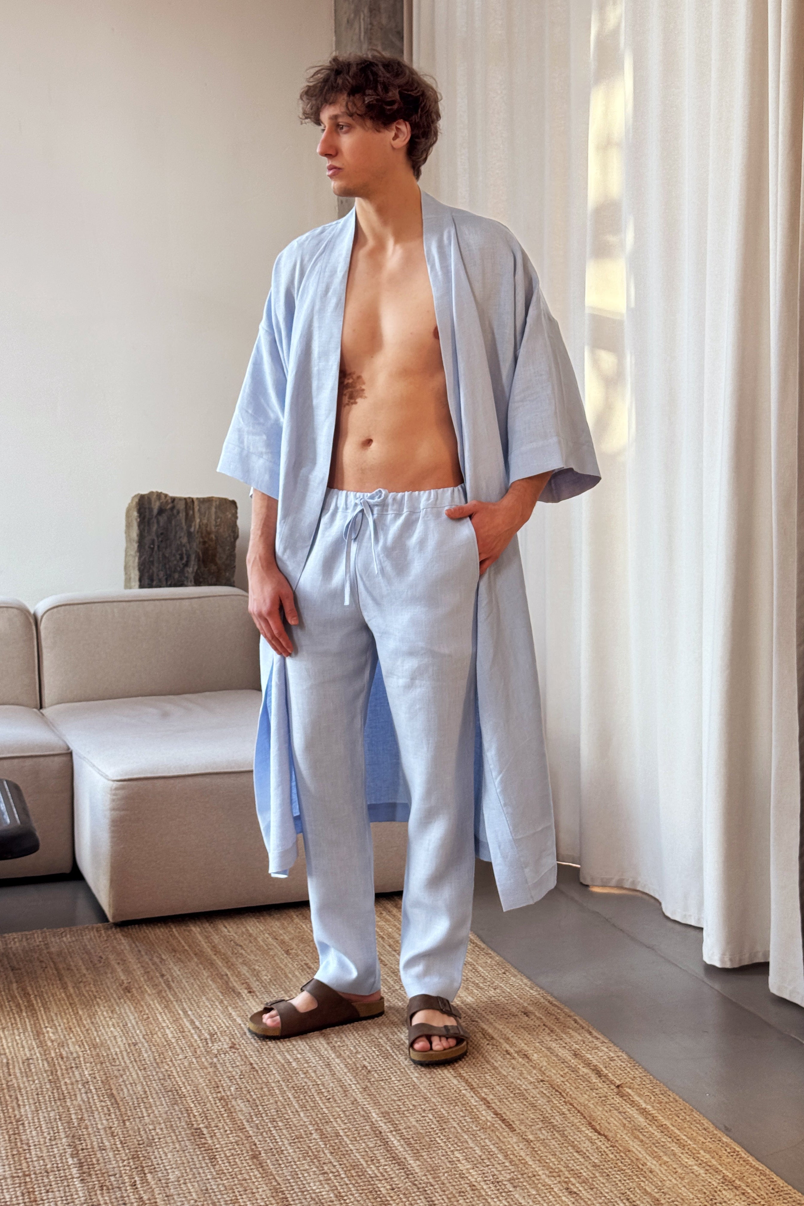 Man wearing a light blue robe and pants in a living room.