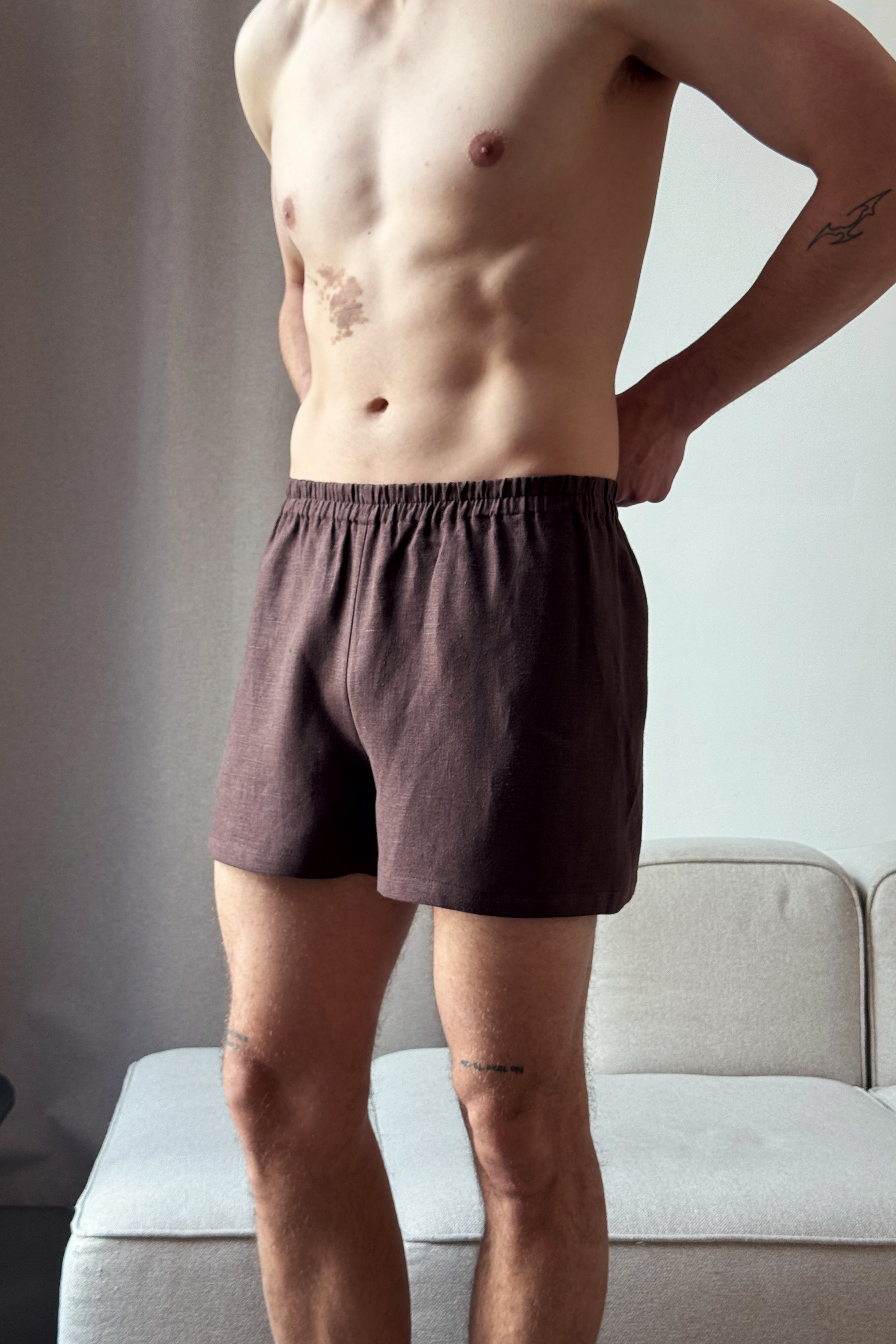 Man wearing brown boxer shorts standing in a room with a neutral background